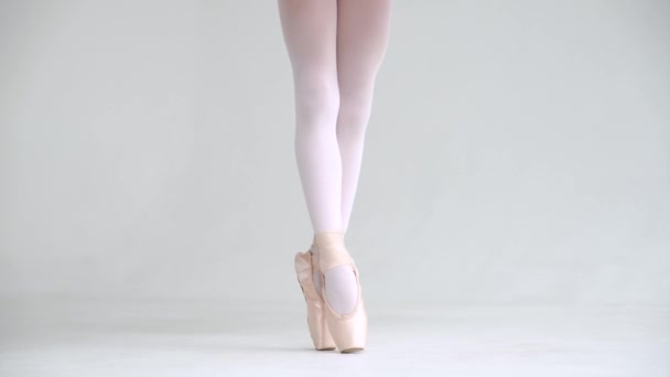 Niña en un tutú blanco, balanceándose en zapatos Pointe, vista de las piernas, fondo blanco. — Vídeos de Stock