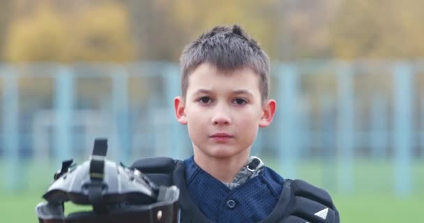 Porträtt av en pojke baseball spelare på en suddig bakgrund, sätter catcher på en skyddande hjälm och tittar på kameran, en allvarlig look, 4k slow motion. — Stockvideo