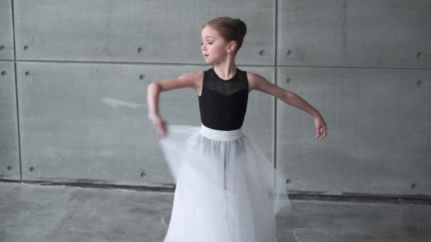 Elegant klein meisje in een zwart-wit tutu jurk, dansballet en choreografische elementen uit te voeren op een grijze achtergrond, repetitie. — Stockvideo