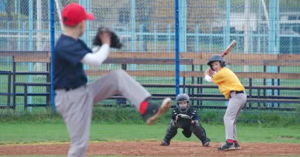 Chłopcy grają w baseball w szkole, miotacz rzuca piłkę w stronę pałkarza, łapacz łapie szybką piłkę. — Wideo stockowe