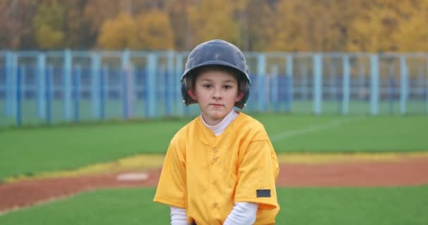 Potret seorang anak laki-laki pemain bisbol dengan latar belakang yang kabur, pemukul memegang tongkat baseball di tangannya dan melihat ke kamera, gerakan lambat 4k. — Stok Video