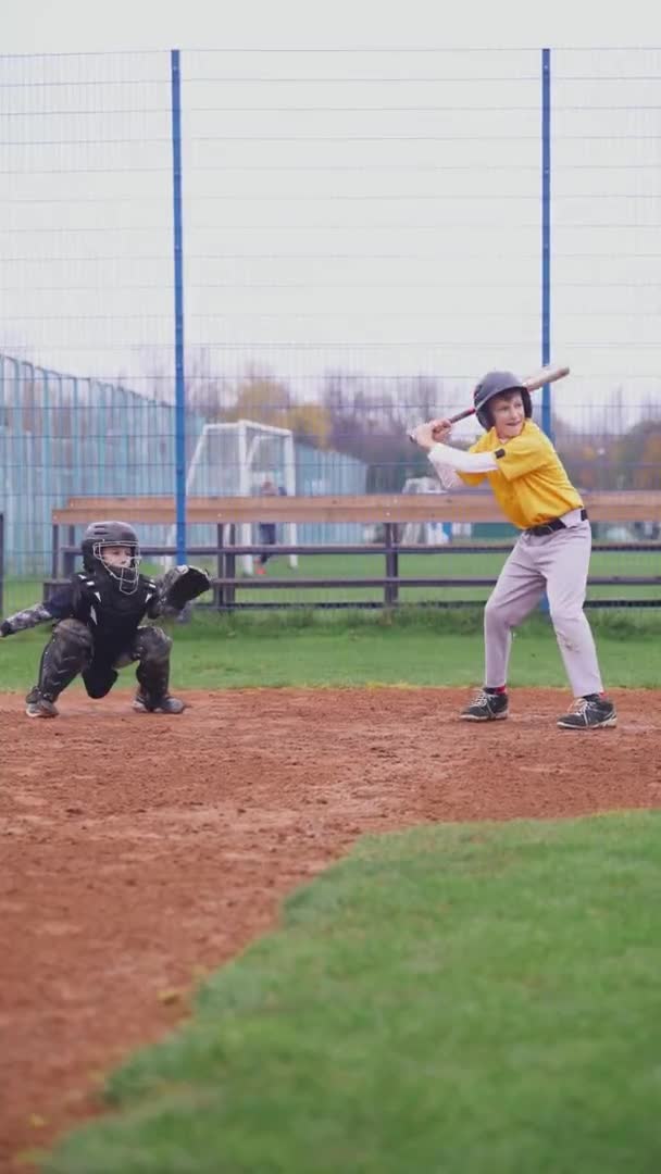 Torneio de beisebol na escola, os meninos jogam beisebol, o rebatedor acerta com sucesso uma bola voadora e corre para a base, vídeo vertical 4k. — Vídeo de Stock