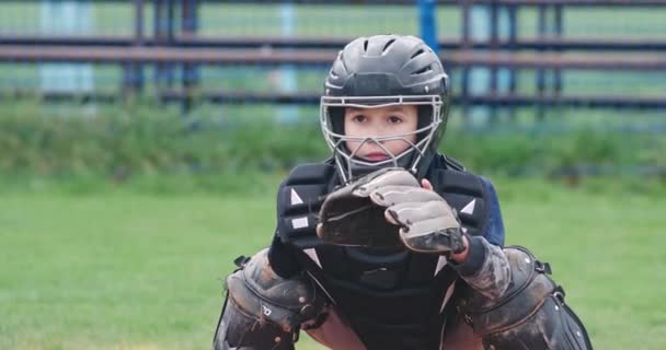 Porträtt av en pojke baseball spelare på en suddig bakgrund, fångar catcher i skyddsutrustning en flygande fastball till handsken, 4k slow motion. — Stockvideo