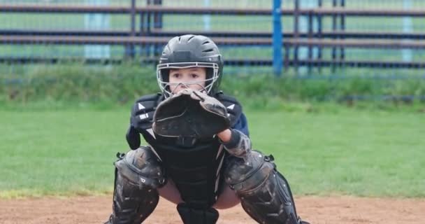 ぼやけた背景に少年野球選手の肖像、保護具のキャッチャーは、手袋、 4kスローモーションに飛んで速いボールをキャッチします. — ストック動画