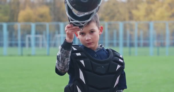 Portré egy fiú baseball játékos homályos háttérrel, a elkapó felvesz egy védő sisakot, és néz a kamera, komoly megjelenés, 4k lassított felvétel. — Stock videók