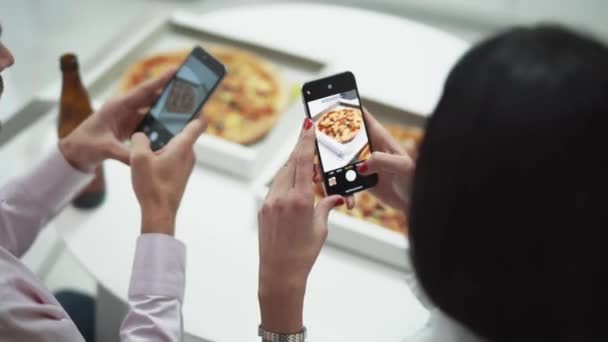 Home party, un jeune couple assis à la table dans la cuisine et prenant des photos de pizza sur smartphones. — Video