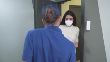 Koruyucu maskeli ve eldivenli kurye müşterilere pizza dağıtıyor. Virüs salgını durumunda yiyecek teslimatı yapılıyor. Erkek pizza kutularını bir kadına veriyor..