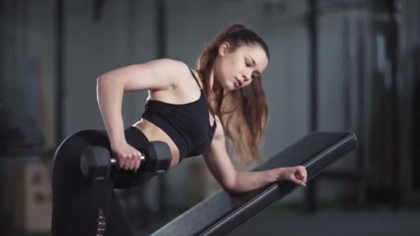Молодая женщина в тренажерном зале, девушка поднимает гантель в наклоне, тренировки мышц с гирями. — стоковое видео