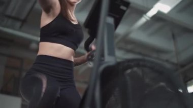 Spor salonunda bir kadın, eliptik bisiklet simülatörü, aerobik egzersiz ve dayanıklılık eğitimi, düşük açılı görüş..