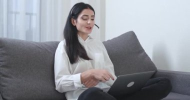 Serbest çalışan bir kadın kanepede oturuyor ve bir dizüstü bilgisayar üzerinde çalışıyor, video görüşmesi, teknik destek veren bir kadın bir konferans görüşmesinde konuşuyor, evden uzaktan kumandalı bir iş..