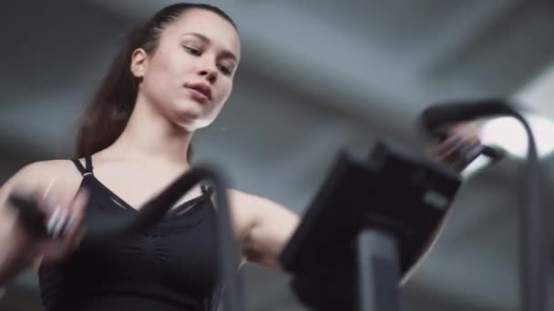 Młoda kobieta trenuje na eliptycznym symulatorze roweru, ćwiczy aerobik i trening wytrzymałościowy, widok z niskiego kąta. — Wideo stockowe