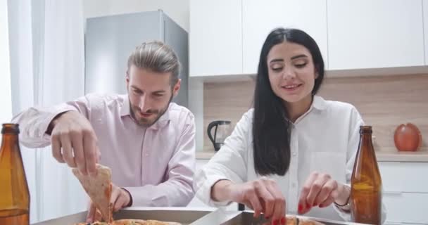 Σπίτι κόμμα, ένα νεαρό ζευγάρι κάθεται στην κουζίνα και τρώει πίτσα, το μεσημεριανό γεύμα, ο τύπος και το κορίτσι σε αυτο-απομόνωση. — Αρχείο Βίντεο