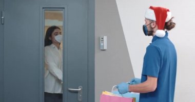 Koruyucu maskeli ve eldivenli kurye müşterilere hediyeler dağıtır. Virüs salgını durumunda teslimat süreci. Erkek kadına hediye paketleri verir..