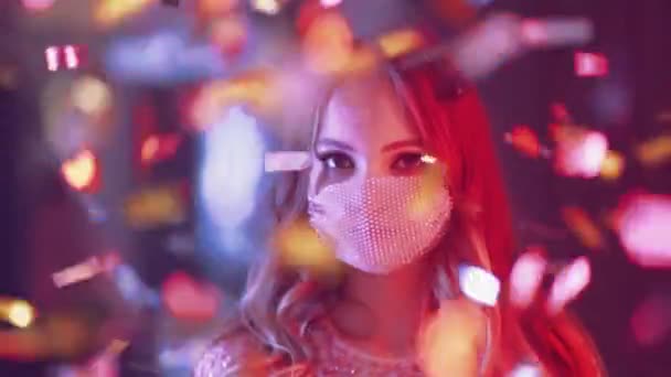 Party, beautiful female wearing protective mask in the night club, stands and looks at the camera, golden confetti flying in the air, neon light, party during the pandemic, 4k slow motion. — Stock Video