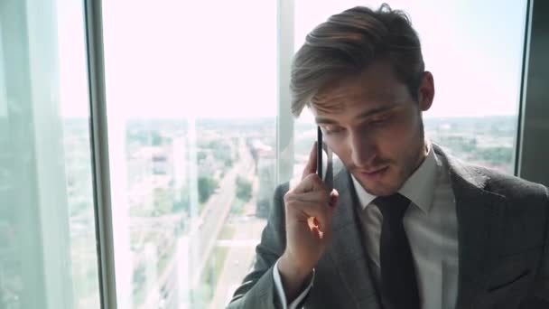 Jovem empresário em um terno fala em um telefone celular e monta em um elevador panorâmico em um arranha-céu. — Vídeo de Stock