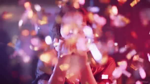 Портрет гламурної жінки в нічному клубі, молода жінка дме конфетті і посміхається, золота конфетті літає в повітрі, неонове світло, 4k повільний рух . — стокове відео
