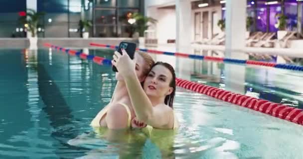 Kvinnor i poolen, två vackra flickor i gula baddräkter tar en selfie på en smartphone när de är i poolen. — Stockvideo