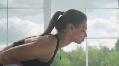 Genç bayan ışıkla dolu beyaz bir odada yoga yapıyor, kız büyük pencerenin yanında kaslarını esnetiyor..