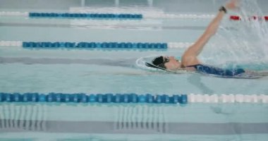 Sırtüstü yüzen genç bir kadın, havuzda yüzen bir yüzücü, havuzda yüzen ve antrenman yapan bir kadın, ağır çekim..