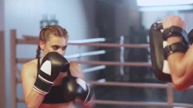 Kadın boksör yumrukları ve savunmayı eğitiyor, odaklanma eldivenlerini yumrukluyor, antrenörle boks salonunda antrenman yapıyor, agresif..