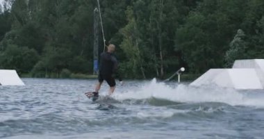 Ormanın yakınındaki bir gölde sörf yapmak, adam suda sörf yapmak, sörf tahtasında sörf yapmak, arka manzara, 4k Slow Motion.