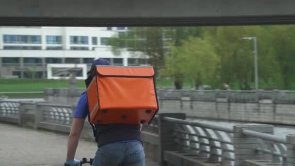 Entrega de comida en las condiciones de una pandemia viral, mensajero en máscara médica con una mochila termo monta una bicicleta para el cliente. — Vídeos de Stock