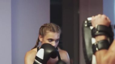 Kadın boksör yumrukları ve savunmayı eğitiyor, odaklanma eldivenlerini yumrukluyor, antrenörle boks salonunda antrenman yapıyor, agresif..