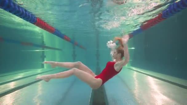 Professionelle Schwimmerin, junge Frau in rotem Badeanzug führt die Elemente des Synchronschwimmens aus, schöner Tanz unter Wasser. — Stockvideo