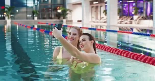 若いです女性でプール,二人の美しい女の子で黄色の水着で自画撮りスマートフォン,女の子の笑顔とポーズのためにカメラ. — ストック動画