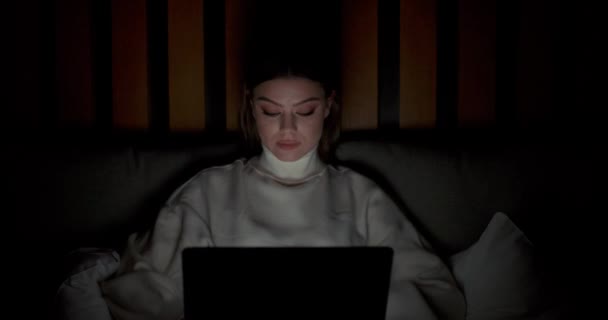 침대에 누워 노트북을 만들고 키보드로 문자를 쓰고 밤 시간, 집에서 멀리 떨어진 곳에서 일하는 젊은 여자. — 비디오