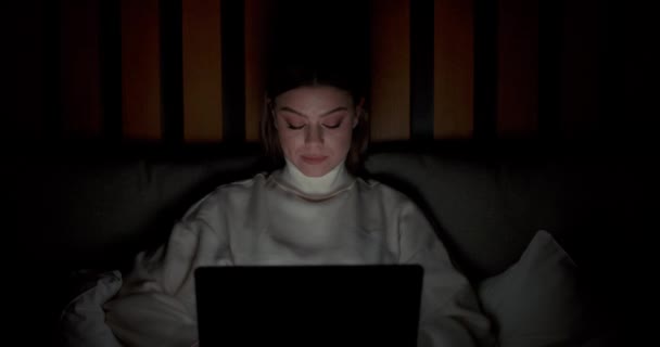Ung kvinna som ligger på sängen och arbetar på en bärbar dator, skriver text på tangentbordet, nattetid, distansarbete hemifrån. — Stockvideo