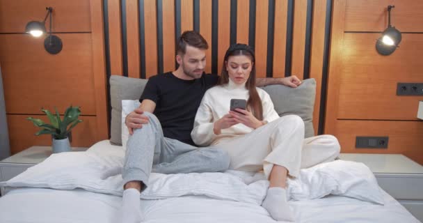 Jovem casal senta-se no sofá na sala de estar, jogo feminino em um smartphone, menina ganha o jogo, emoções de vitória, auto-isolamento. — Vídeo de Stock