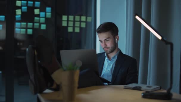 Mladý kancelářský pracovník pracuje dlouho do noci, unavený muž s laptopem na klíně pracuje přesčas, noční práce. — Stock video