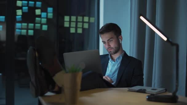 Mladý muž finanční analytik pracuje pozdě, unavený muž s notebookem na klíně pracuje přesčas, noční práce. — Stock video