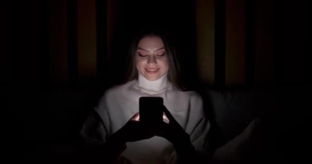 Mladá žena ležící na posteli a používá smartphone, typy text, noční, on-line komunikace, self-izolace. — Stock video