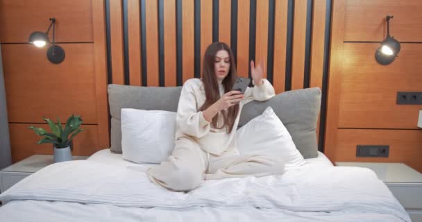 Giovane donna si siede sul letto, gioco femminile su uno smartphone e vince la partita, emozioni di vittoria, auto-isolamento. — Video Stock