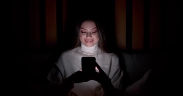Jonge vrouw liggend op het bed en maakt gebruik van smartphone, types tekst, 's nachts, online communicatie, zelf-isolatie. — Stockvideo