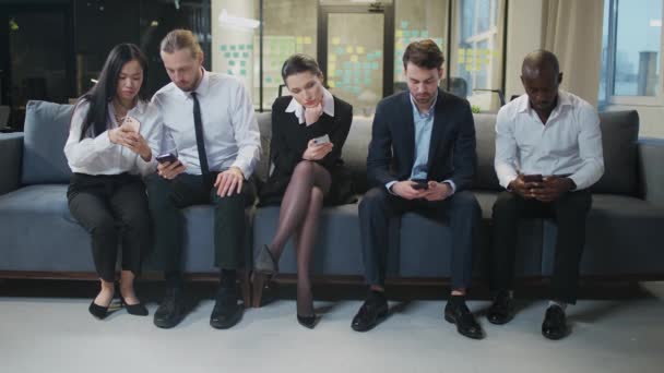 Groupe de personnes assises dans la salle d'attente et utilisent des smartphones, l'équipe de bureau attend le début de la conférence, les hommes et les femmes s'assoient sur des chaises. — Video