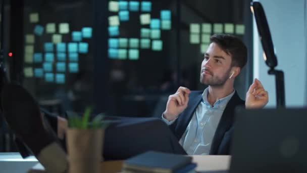 Un gars joyeux portant un casque sans fil écoute de la musique sur le lieu de travail au bureau, une bonne humeur, un directeur financier s'amuse au travail. — Video