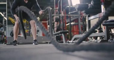 Spor salonundaki atletik adam, savaş halatlarıyla tatbikatlar yapıyor, dayanıklılık eğitimi alıyor..