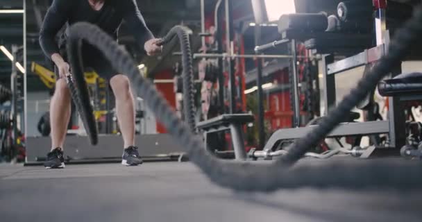 Friidrott man i ett gym, utför övningar med stridsrep, crossfit uthållighetsträning. — Stockvideo