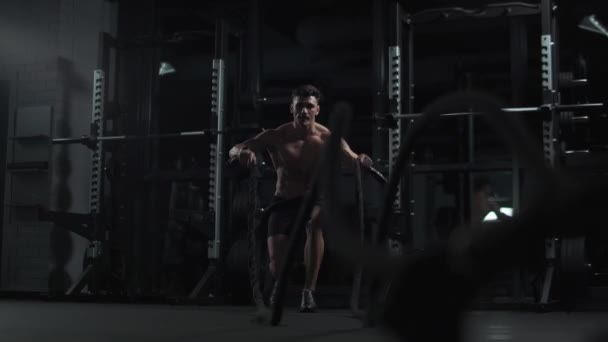 Атлетик выполняет упражнения с боевыми канатами, выносливость тренировки в тренажерном зале, кинематографический свет, 4k замедленной съемки. — стоковое видео