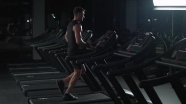 Koşu bandında koşan genç bir sporcu, spor salonunda aerobik egzersiz ve dayanıklılık eğitimi, gece antrenmanı, 4k ağır çekim.