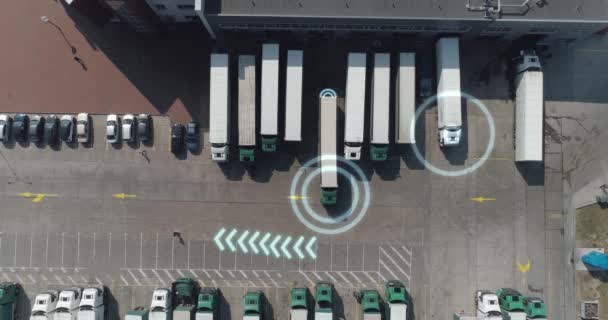 Здания логистического центра рядом с автомагистралью, грузовик покидает стоянку, искусственный интеллект отслеживает грузовики, движение графики, вид с высоты, большое количество грузовиков на парковке рядом — стоковое видео