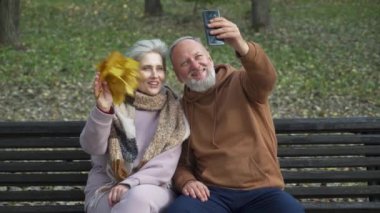 Yaşlı çift bir orman parkında bankta oturur ve akıllı bir telefondan selfie çekerler. Gri saçlı erkek ve kadın konferans görüşmesiyle iletişim kurarlar..