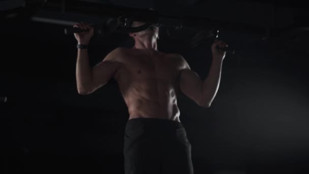 Hombre atlético realiza pull-ups en la barra horizontal, entrenamiento de fuerza en el gimnasio, luz cinematográfica. — Vídeos de Stock