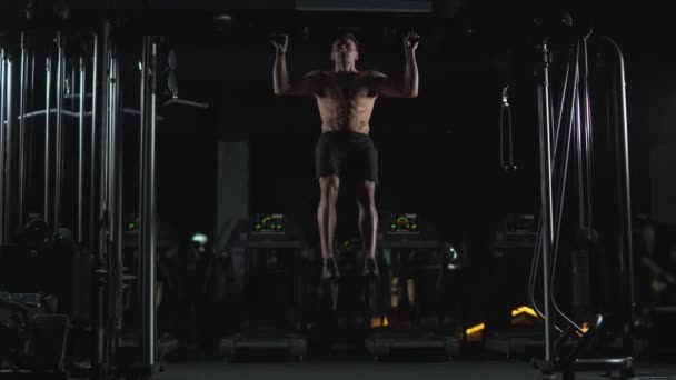 Hombre atlético realiza pull-ups en la barra horizontal, entrenamiento de fuerza en el gimnasio, luz cinematográfica. — Vídeos de Stock