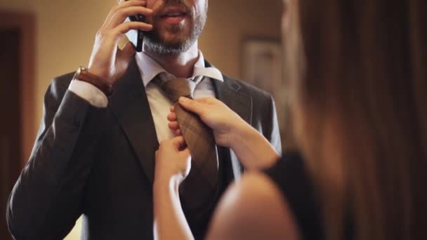 Mladý muž v obleku mluví na mobilním telefonu, žena váže kravatu k muži, služební cesta, interiér hotelu. — Stock video