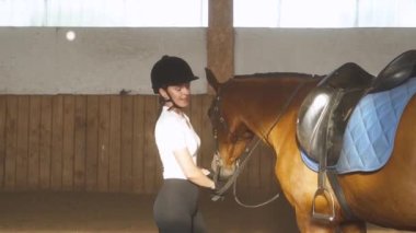 Genç bir kadın ata biner ve üstü örtülü bir hangarda ata biner..