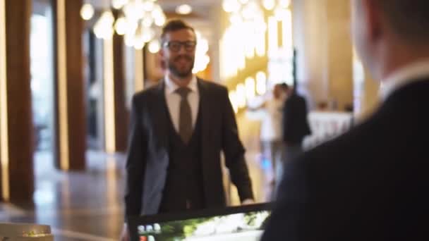 Uomo d'affari in giacca e cravatta che trasporta una valigia uomo va alla reception dell'hotel e riceve una chiave magnetica dalla camera, viaggio d'affari. — Video Stock